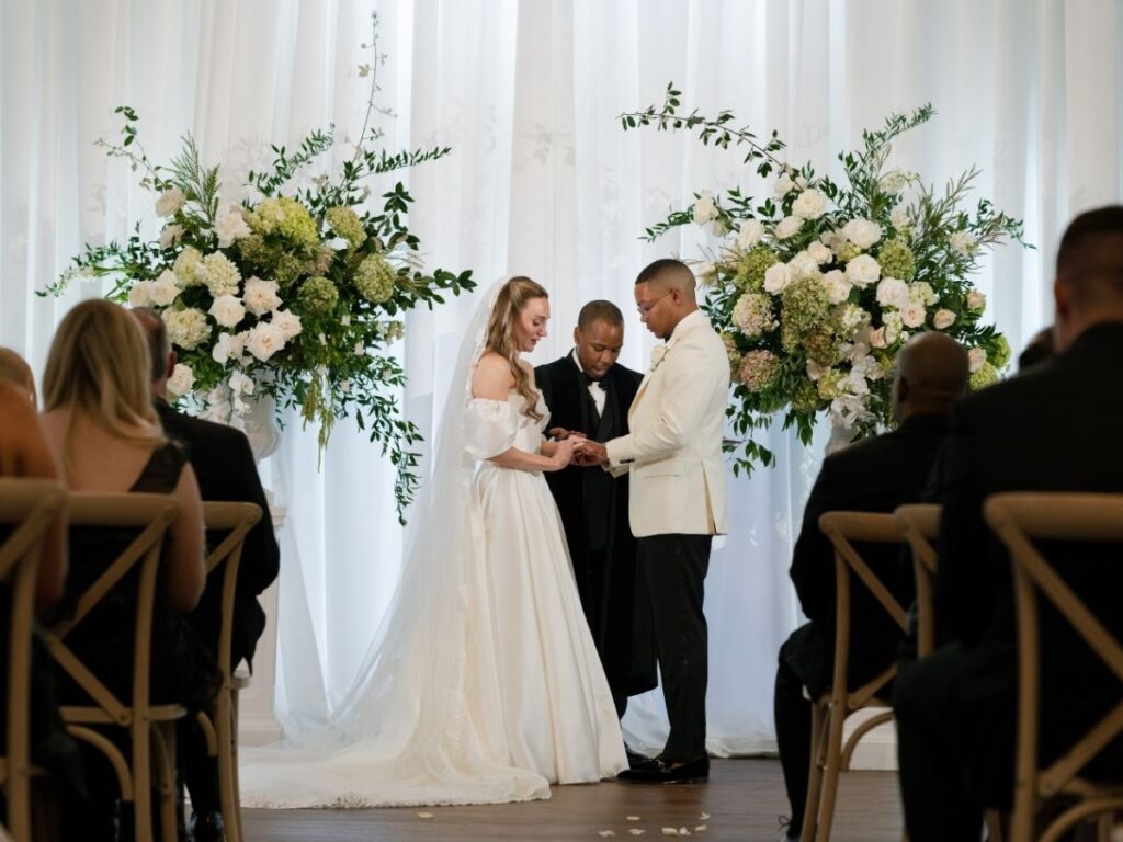 Bride and groom at ceremony site with white drapery and lush white and green florals