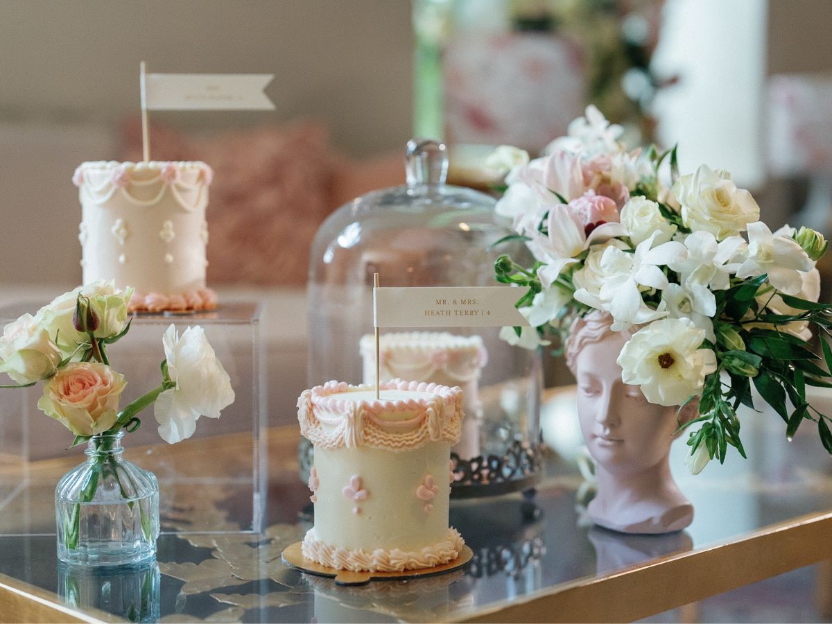 French petite cakes used for a wedding escort display atop a table with florals and a Versailles-inspired sculpture of a female head